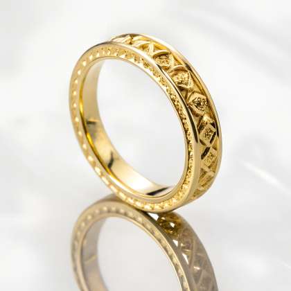 Features a highly detailed golden ring with intricate ornamentation, reflecting on a glossy surface against a subtle background. High-resolution close-up captures luxury jewelry.